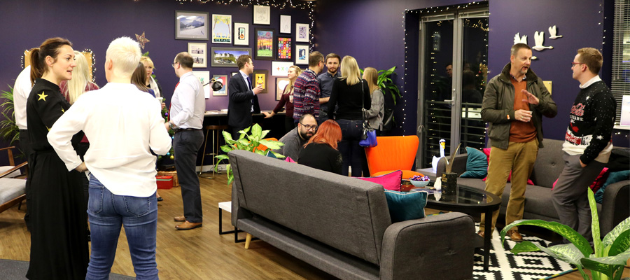 Group of people standing around inside an office talking and socialising 