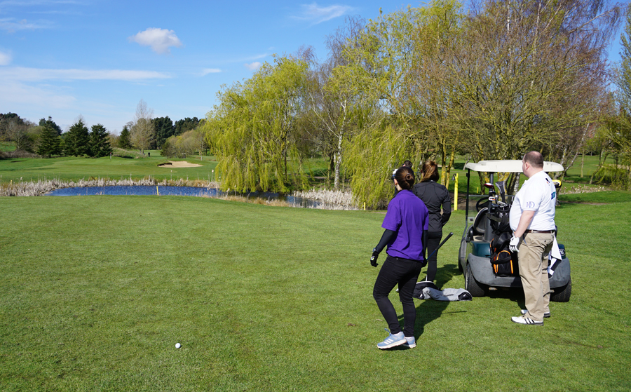 People standing on golf course in front of pond
