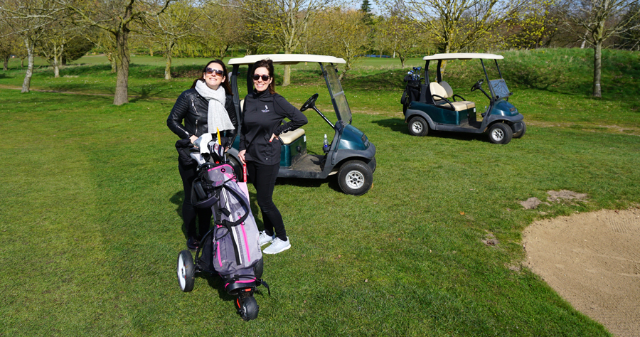 Two ladies standing in front of a set of golf clubs