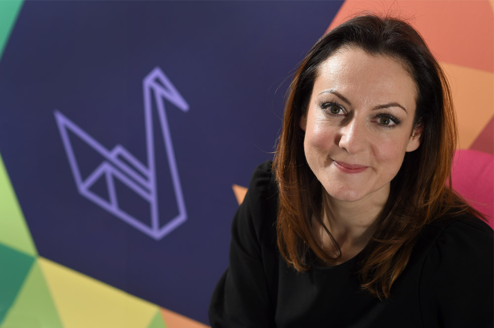 Emily sitting in front of wall with Indigo Swan logo on it